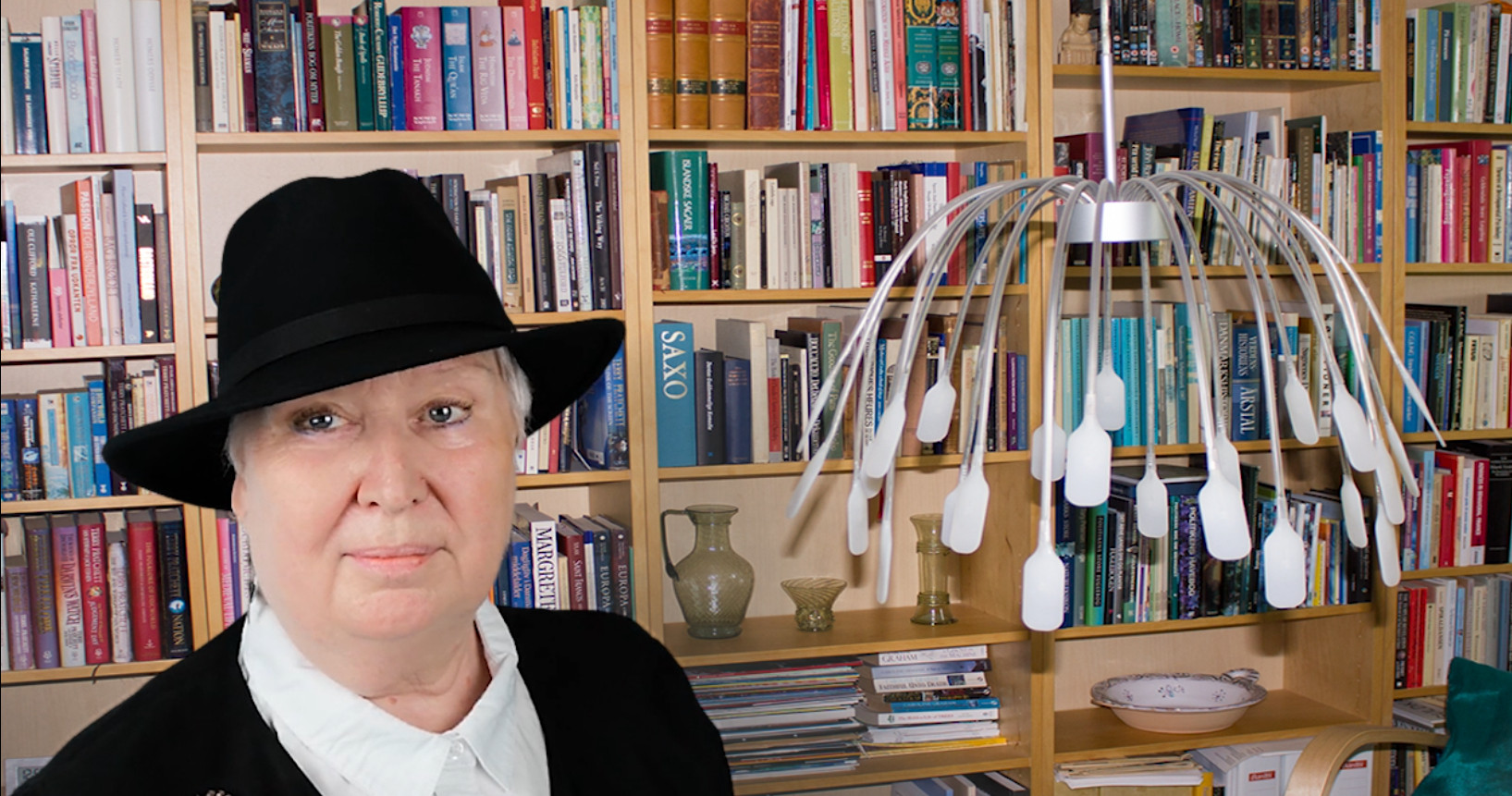 Forfatteren med hat på i dagligstuen med en fyldt reol bagved